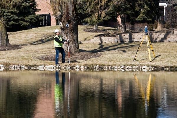 Land surveyor using equipment near a riverbank to recheck property elevations for an updated elevation certificate after flooding

