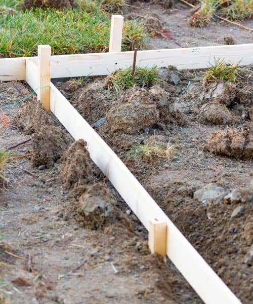 Ground stakes and layout strings marking the footing line for a new block wall