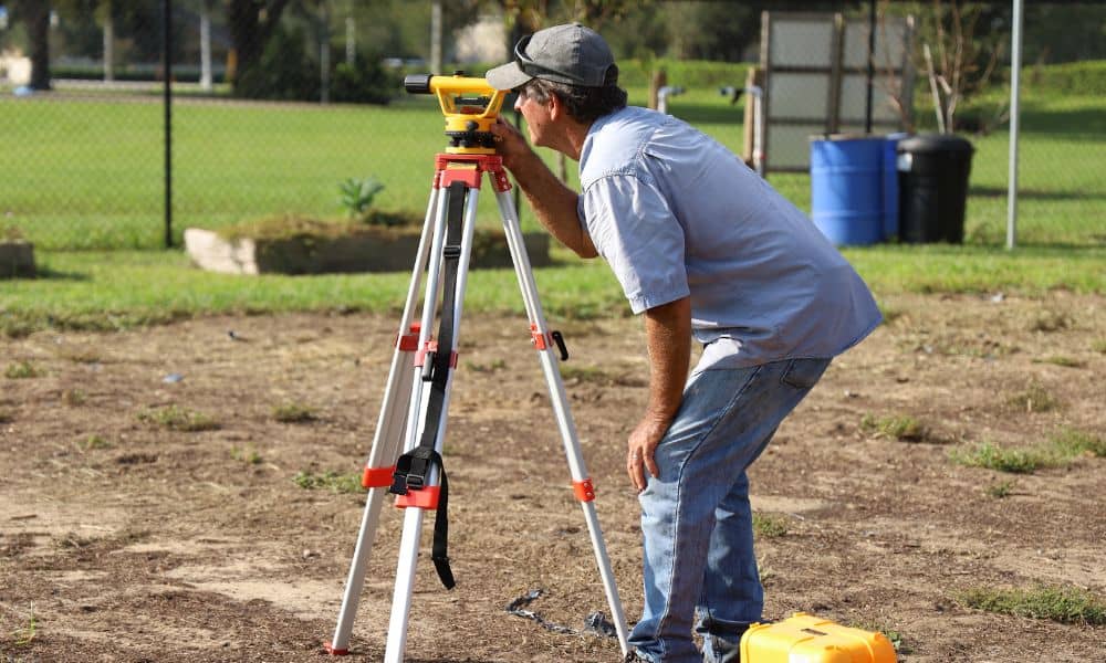 Surveyor setting up equipment in a yard to prepare for a construction staking survey before building a block wall