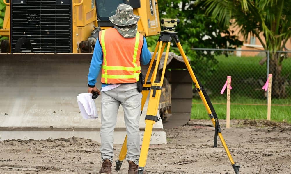Licensed land surveyor measuring ground and building height for a FEMA elevation certificate survey on a residential property