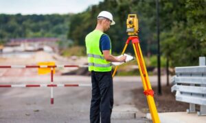 Licensed land surveyor using a total station to measure property boundaries during an alta land title survey on a commercial site