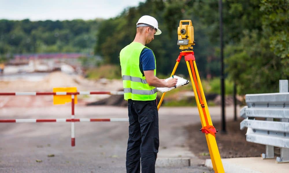 Licensed land surveyor using a total station to measure property boundaries during an alta land title survey on a commercial site
